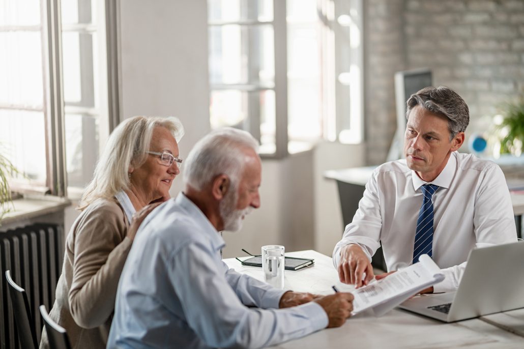 Financial advisor meeting with senior couple and offering them a contract to sign in the office.