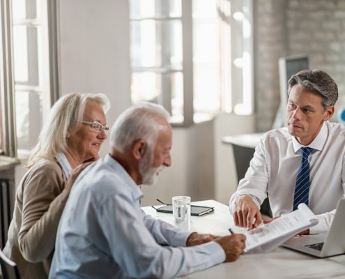 Financial advisor meeting with senior couple and offering them a contract to sign in the office.