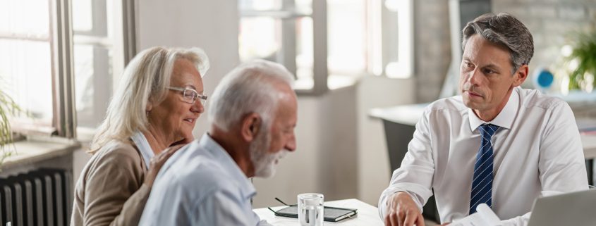 Financial advisor meeting with senior couple and offering them a contract to sign in the office.